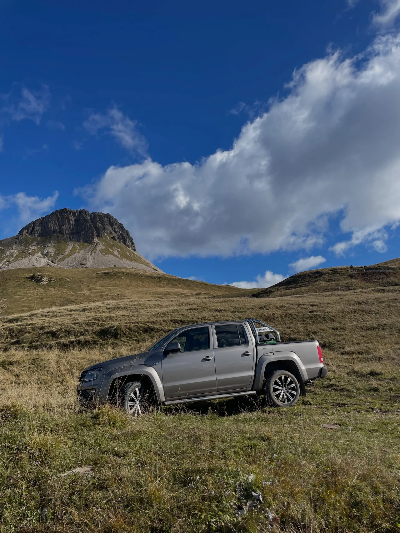 A pickup parked on alpine grass under a blue sky, Pale di San Martino